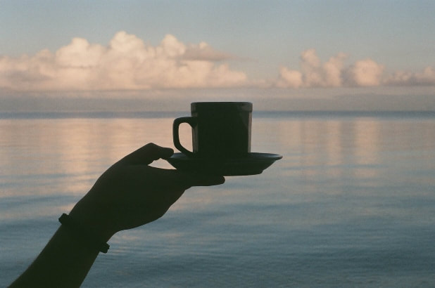 Tea served in cup with saucer, calm water background with clouds.