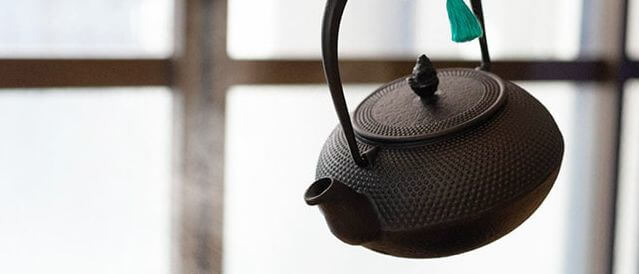 Japanese Iwachu cast iron Tetsubin style teapot, black with hobnails, pouring green tea into which porcelain tea cup.